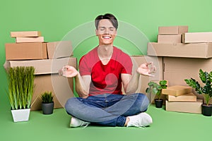 Photo of dreamy cute young guy dressed red t-shirt sitting floor practicing yoga moving new flat smiling isolated green