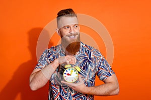 Photo of dreamy positive guy dressed print shirt holding clock lookng emtpy space isolated orange color background