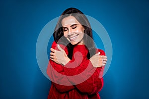 Photo of dreamy pretty young woman dressed red pullover hugging herself smiling closed eyes isolated dark blue color
