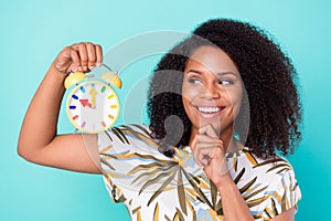 Photo of dreamy shiny dark skin woman dressed blouse holding watch arm chin looking empty space isolated teal color