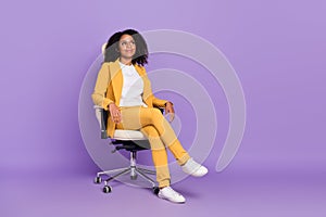 Photo of dreamy shiny woman dressed yellow suit spectacles sitting chair empty space isolated violet color background