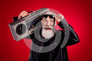 Photo of elderly man happy positive smile hold retro boombox sound rocker hand touch glasses isolated over red color