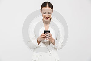 Photo of elegant businesswoman 20s wearing elegant jacket smiling while typing on cell phone