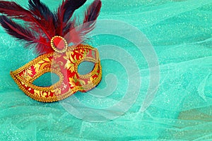 Photo of elegant and delicate red with gold Venetian mask over mint chiffon background