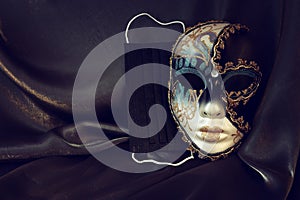 Photo of elegant and delicate Venetian mask over black silk background. Coronavirus prevention concept