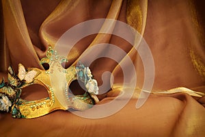 Photo of elegant and delicate Venetian mask over gold silk background