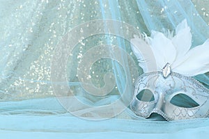 Photo of elegant and delicate white Venetian mask over gold and blue chiffon background