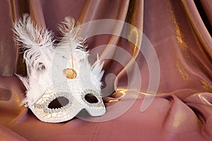 Photo of elegant and delicate white Venetian mask over gold silk background