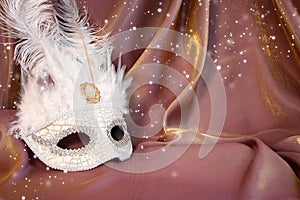Photo of elegant and delicate white Venetian mask over gold silk background