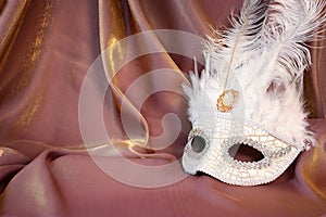 Photo of elegant and delicate white Venetian mask over gold silk background