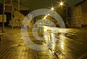 Empty wet street at night illuminated by lamps