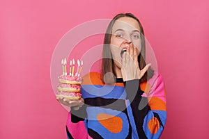 Photo of excited amazed woman with brown hair wearing stylish jumper, covering mouth with palm, having surprise on her birthday