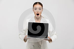 Photo of excited businesswoman 20s wearing elegant jacket holding laptop and showing black screen