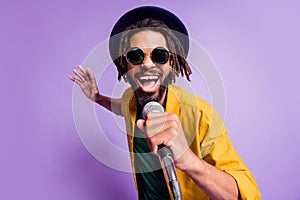 Photo of excited carefree dark skin guy arm hold mic open mouth singing loud isolated on violet color background