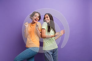 Photo of excited funky girls dressed t-shirts dancing having fun smiling isolated purple color background