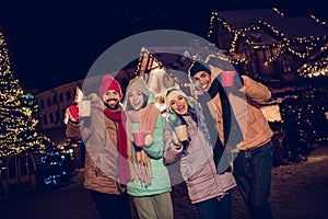 Photo of excited funky two couples dressed coats drinking x-mas rising mulled wine mugs outdoors urban fair park