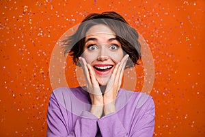 Photo of excited funny girl dressed purple pullover arms cheeks air flying glitter isolated orange color background