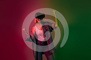 Photo of excited millennial lady playing video game on digital goggles winning isolated gradient neon color background