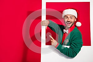 Photo of excited pretty guy dressed xmas green cardigan holding photo frame pointing empty space isolated red color