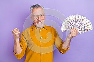Photo of excited senior man rejoice fists hands money benefit income isolated over violet color background