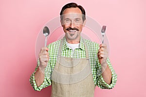 Photo of excited starving young guy dressed beige apron plaid shirt smiling holding fork spoon isolated light pastel