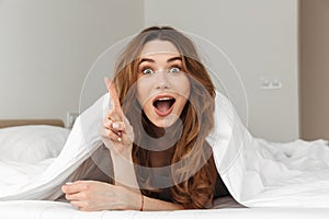 Photo of excited woman 20s lying in bed under white blanket in b