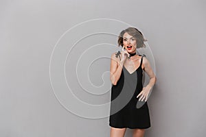 Photo of excited woman 20s wearing black dress smiling at camera