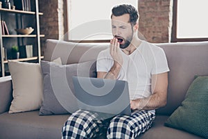 Photo of exhausted man sit divan work remote laptop tired prepare startup progress innovation report yawn mouth hand