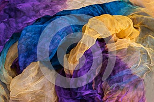 A photo of fabric dyed yellow, blue, purple colours and laid out in an abstract form for use as a background