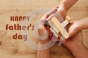 Photo of father and little child holding together wooden toy plane. Happy father`s day and holiday concept. top view, above