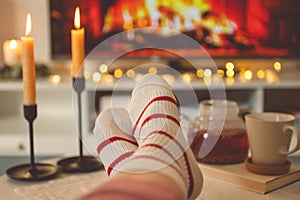Photo of feet in striped socks on side table with candles, teapot and cup  bevor fireplace