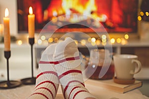 Photo of feet in striped socks on side table with candles, teapot and cup  bevor fireplace