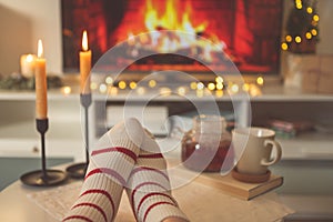 Photo of feet in striped socks on side table with candles, teapot and cup  bevor fireplace imitation