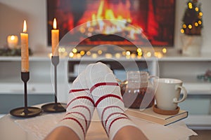 Photo of feet in striped socks on side table with candles, teapot and cup  bevor fireplace imitation