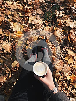 Photo of female legs against a background of yellow leaves with coffee. Vertical shot.