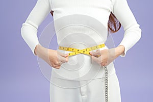 Photo of a fit and healthy young lady measuring her waist with a tape measure in centimeters and millimeters photo
