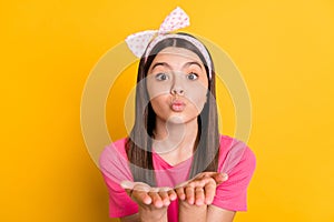 Photo of flirty funny small schoolgirl dressed pink t-shirt sending you arms kiss isolated yellow color background