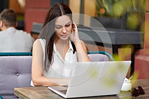 Photo fo concetrated female freelancer watches tutorial online, uses laptop computer for work, sits at table in outdoor cafeteria,