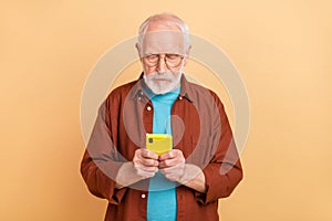 Photo of focused concentrated addicted to smartphone grandpa chatting with his wife isolated on beige color background