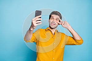 Photo of foolish ridiculous man showing v-sign sticking toungue out holding phone taking selfie behaving childish