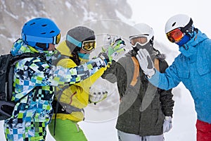 Photo of four happy snowboarders in helmet doing handshake on mountains background .