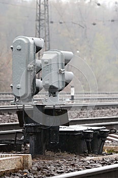 Photo of a fragment of a railway track with a small traffic light in rainy weather