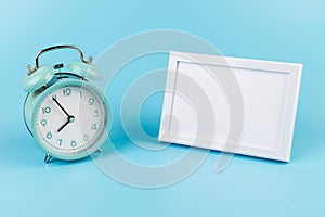 Photo frame and blue alarm clock on blue background with copy space