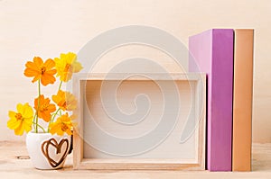 Photo frame with books and flowers on the wooden table