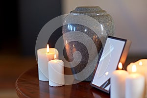 Photo frame, cremation urn and candles on table