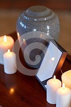 Photo frame, cremation urn and candles on table