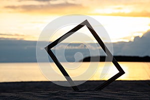 Photo frame in sand on the beach. Beautiful sunset background.