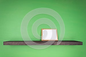 The photo frame stands on a dark color shelf with a tree texture that is attached to the green wall