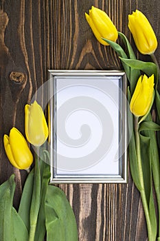 Photo frame on a wooden background in an orchestration of yellow tulips