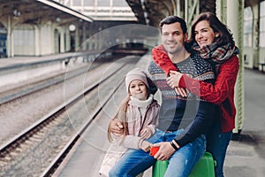 Photo of friendly family have good relationship, have trip during vacation, pose at platform of railway station. Lovely woman